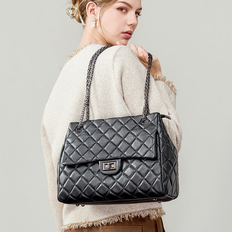 Woman holding a black quilted handbag with a chain strap against a gray background