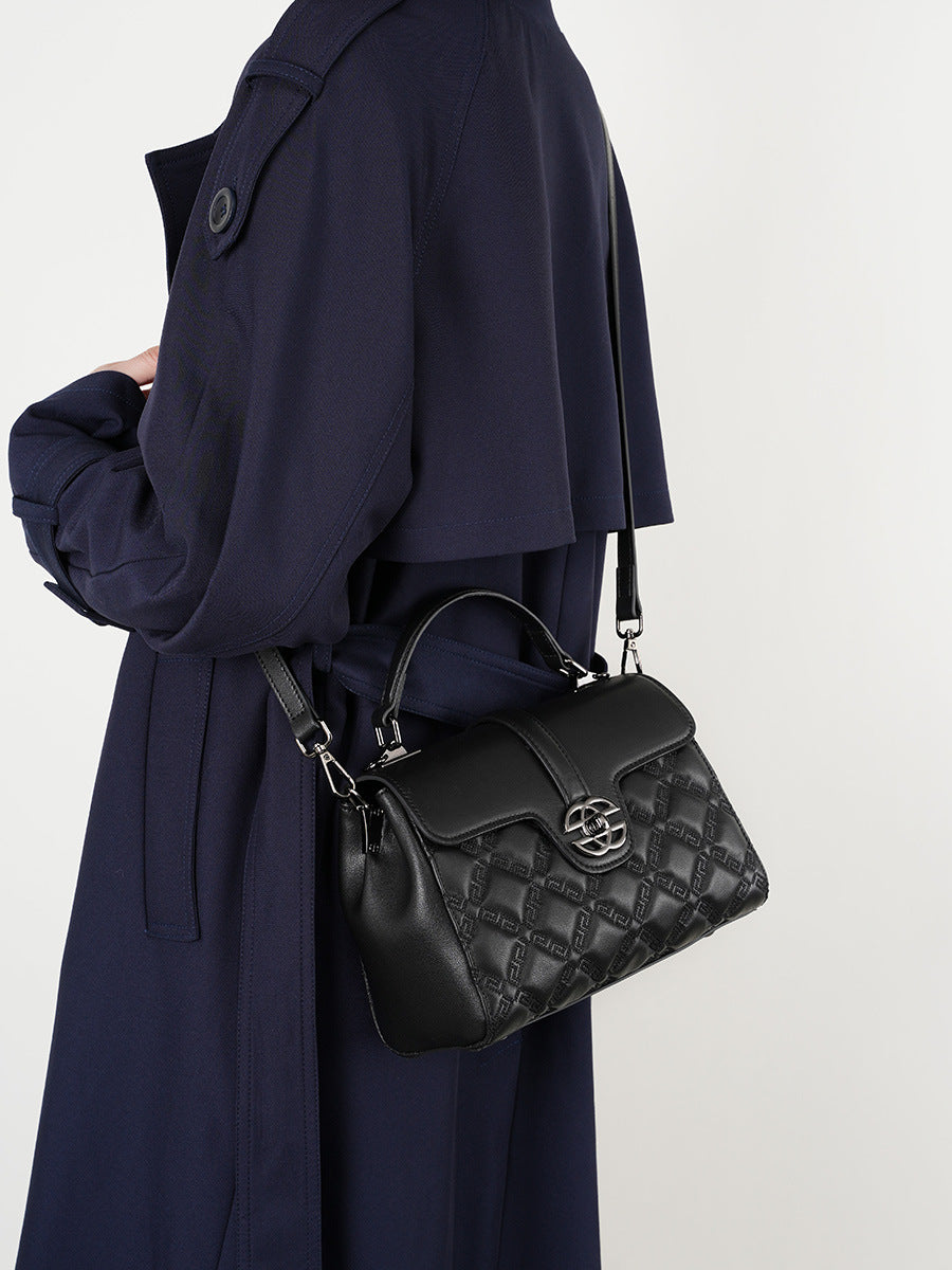 Person wearing a navy coat with a black quilted handbag on a white background
