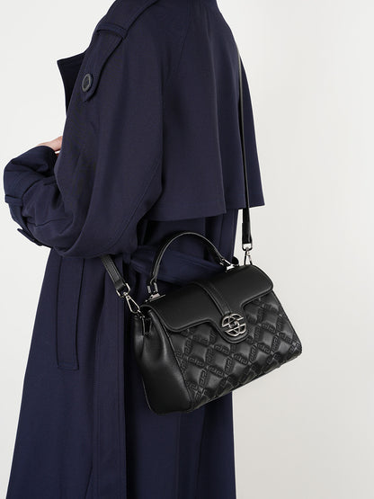 Person wearing a navy coat with a black quilted handbag on a white background
