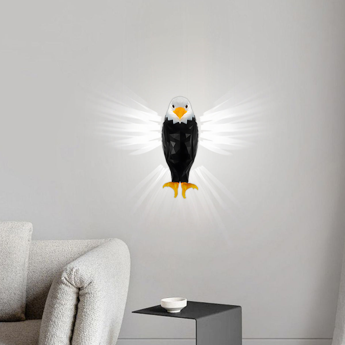 A wall-mounted eagle night light with glowing white wings, shown lit on a light gray wall above a sofa in a modern living room setting.