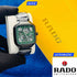 Rado watch held by a gloved hand with a yellow and blue background