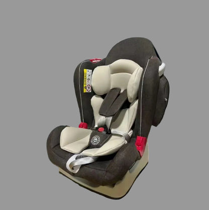 A child car seat with dark brown fabric and beige padding, shown on a gray studio background with dramatic colored lighting.