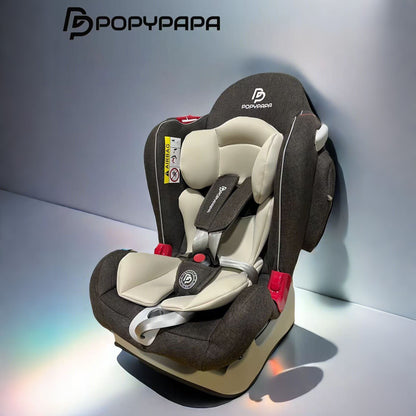  infant car seat shown in a studio setting. The car seat features a dark brown textured fabric shell with cream-colored inner padding and harness straps, accented by small red plastic safety components.