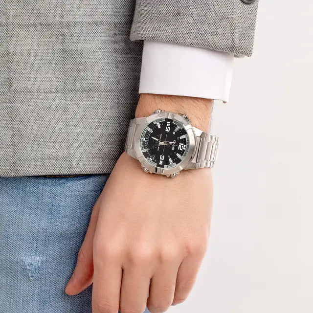 Person wearing a silver watch with a black face on a plain background