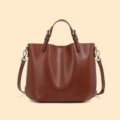 A brown leather tote bag with top handles and a detachable shoulder strap, shown against a solid light beige background.