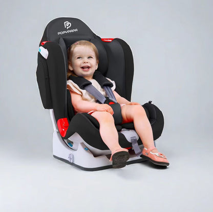 A smiling toddler is seated in a black and gray Popvava car seat with red accents, photographed on a clean light gray studio background.