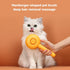 A white long-haired cat sits against a warm orange background while a person holds a bright yellow pet grooming brush in front of its face. White text at the top reads, &