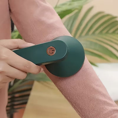 A close-up of a person using an electric arm waxing device on their forearm. The device is dark green with a copper-colored power button, and the person is wearing a dusty pink long-sleeve top.