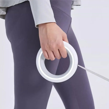 A close-up of a person wearing dark gray leggings and a light gray long-sleeve top, holding a white circular ring light with a thin power cord visible.