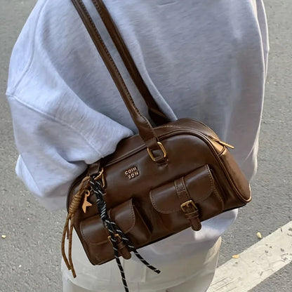 Brown leather bag with gold accents worn by a person in a light blue shirt.